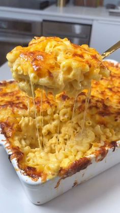 a spoon is lifting some macaroni and cheese out of the casserole