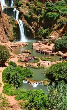 the waterfall is surrounded by lush green trees and people on boats in the water below