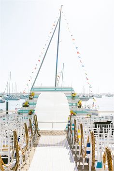 an outdoor ceremony setup with white chairs and colorful ribbons on the aisle, along with flags flying in the wind