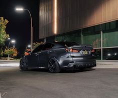 a grey car parked in front of a building at night with street lights on the side