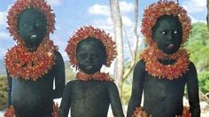 three black children with orange wreaths on their heads and body are standing in front of trees