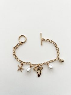 Gold charm bracelet. Charms include pearls, starfish, bow and acorn. Toggle Clasp. Gold Toggle Bracelet, How To Make A Charm Bracelet, Gold Pandora Bracelet, Aesthetic Bracelets, Charm Bracelet Charms, Pearl Charm Bracelet, Bracelet Packaging, Gold Girl, Pink Canvas