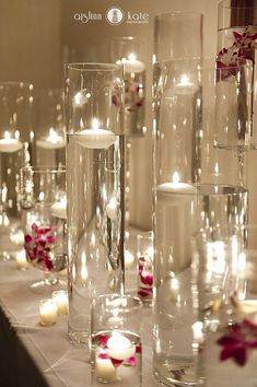 candles are lit on the table with flowers and petals in vases next to them