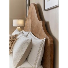 a wooden headboard with white pillows in a bedroom next to a lamp and pictures on the wall