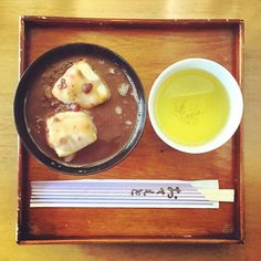 a bowl of soup and some kind of food on a wooden tray with chopsticks