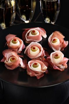 ham wrapped in prosciutto on a black plate with glasses of champagne behind it