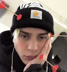 a young man wearing headphones and a beanie with hearts on it, is looking at the camera