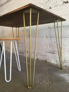 two tables with metal legs and wooden top in front of a brick wall, one has a sign on it