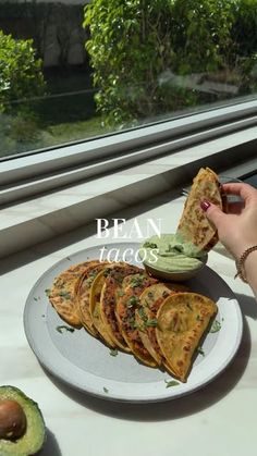 a person holding a piece of bread with guacamole and avocado on the side