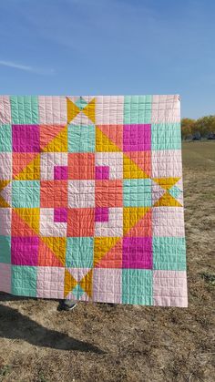 a colorful quilt is hanging on a clothes line in the middle of an open field