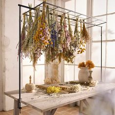 dried flowers are hanging from a rack on a table in front of an open window