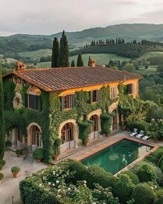 an outdoor swimming pool surrounded by greenery in front of a large house with a stone roof