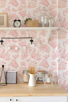 a kitchen with pink coral wallpaper and white cupboards, shelves above the counter