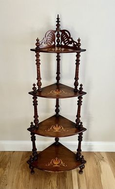 three tiered wooden shelf with carvings on the top and bottom, in front of a white wall