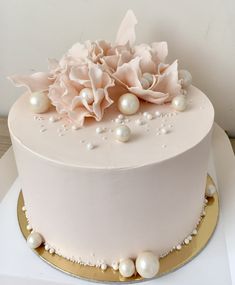 a white cake with pink flowers and pearls on the top is sitting on a gold plate