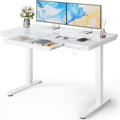 a computer desk with two monitors on it and a vase full of flowers in front of the monitor