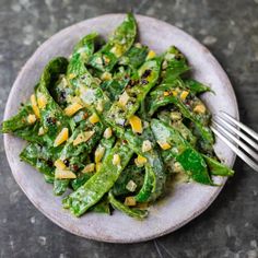 a white plate topped with green vegetables on top of a black tablecloth next to a fork