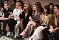 many people are sitting in the front row at a fashion show and one person is holding her hand up