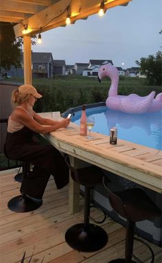 a woman sitting at a table next to an inflatable flamingo drinking wine