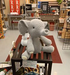 a crocheted elephant sitting on top of a wooden chair in a store aisle