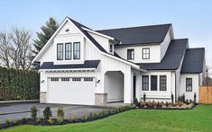 a large white house with black roof and two car garages in the front yard