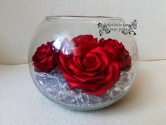 a red rose is in a clear bowl filled with rocks and water on a white surface