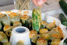 someone is dipping some food into a white dish with cucumbers and other vegetables