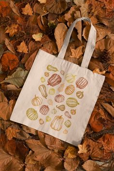 a white bag sitting on top of leaf covered ground with leaves around it and pumpkins painted on the side