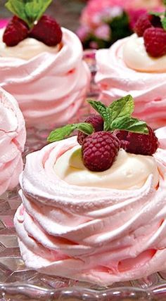 some very pretty pink cupcakes with white frosting and raspberries on top