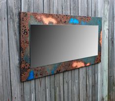 a mirror mounted to the side of a wooden fence with rusted paint on it