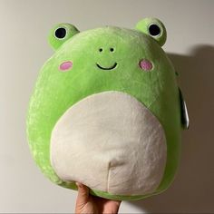 a hand holding up a green stuffed animal with eyes and nose on it's face