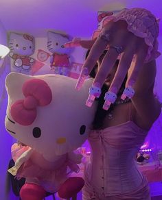 a woman holding up her hand next to a hello kitty stuffed animal in a room