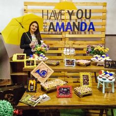 a woman holding an umbrella standing next to a table filled with cakes and cupcakes