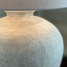 a large white vase with a light on it's side and a lamp in the background