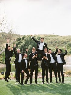 a group of men in tuxedos posing for a photo with their hands up