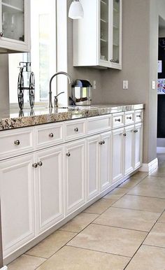 a kitchen with white cabinets and marble counter tops