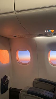 the inside of an airplane with two windows and some bags on the seat, looking out at the sunset