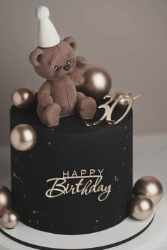 a teddy bear sitting on top of a black and gold birthday cake with pearls around it