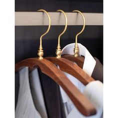 three wooden clothes hangers with brass fittings on each end and two white shirts hanging from them