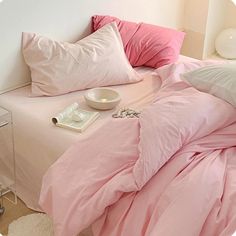 a bed with pink sheets and pillows on top of it next to a night stand