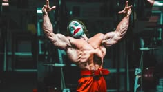 a man with a clown mask and red pants is doing exercises in the gym while holding his hands up