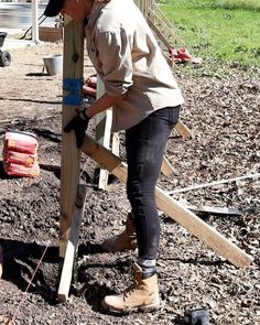 a woman working on a wooden structure in the dirt with tools around her and another person standing next to it