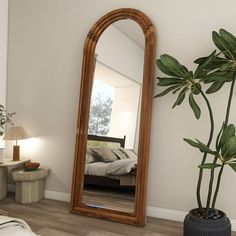 a large mirror sitting on top of a wooden floor next to a plant in a vase