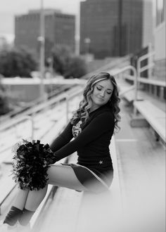 a beautiful young woman sitting on top of a metal bench holding a cheerleader pom - pom