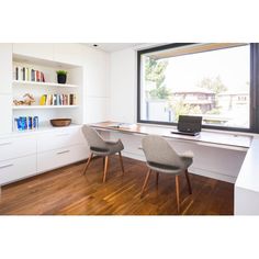 two chairs sitting at a desk in front of a window with bookshelves on it