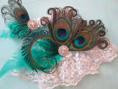 two peacock feathers are on top of a lace garter with green feathers and beads