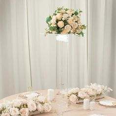 the table is set with white and pink flowers in vases, candles, and napkins