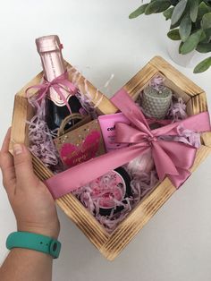 a person holding a wine bottle in a wooden box with pink ribbon around the top