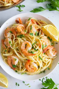 pasta with shrimp and parsley in a white bowl next to lemon wedges on the side