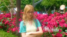 a woman standing in front of flowers with her arms crossed